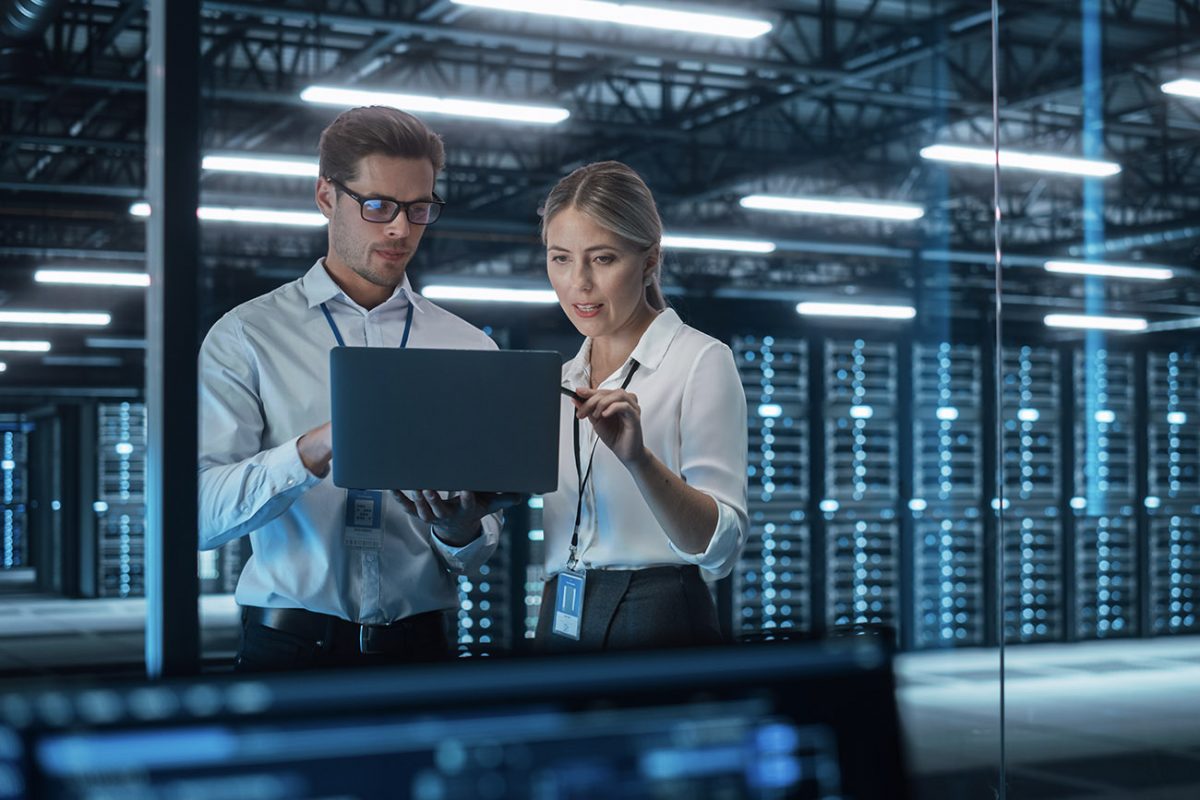 Kollegat, mies ja nainen, keskustelevat konesalissa tietokoneen näyttöä tutkien.