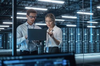 Kollegat, mies ja nainen, keskustelevat konesalissa tietokoneen näyttöä tutkien.
