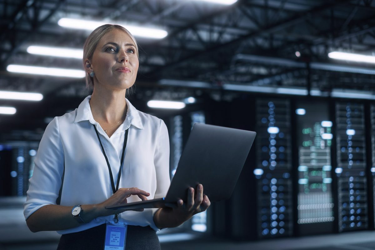 Nainen seisoo kannettava tietokone kädessään konesalissa.