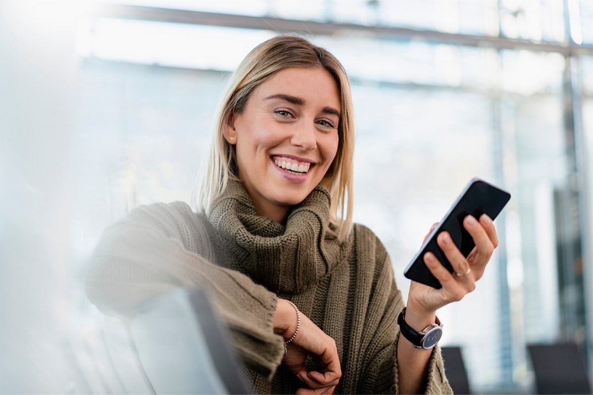 Nainen hymyilee puhelin kädessään.