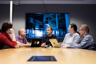 Tiimi keskustelee toimistolla yhteisen pöydän äärellä.